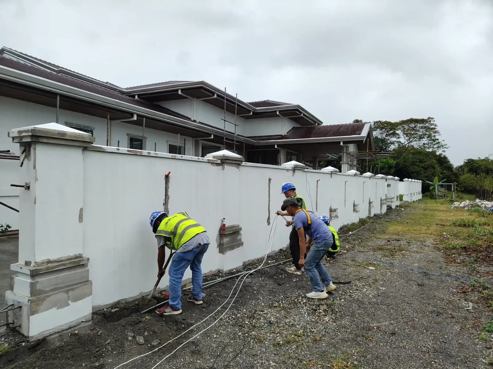 Workers in hi-vis vests pulling cable along a perimeter wall base.